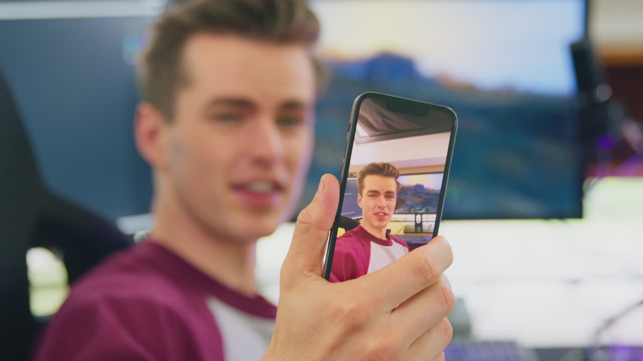 hombre jugando en casa sentado en el escritorio mirando a la cámara transmisión en vivo de juegos filmando en teléfono móvil