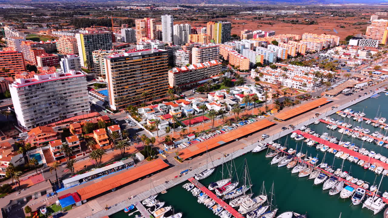 Erhöhter Panoramablick auf einen Yachthafen, Wohngebäude und landwirtschaftliche Felder im Hintergrund. Luftaufnahme einer Küstenstadt mit Hafen und Booten.