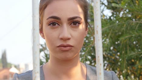 portrait of a beautiful young woman looking out from behind a steel bar gate outdoors