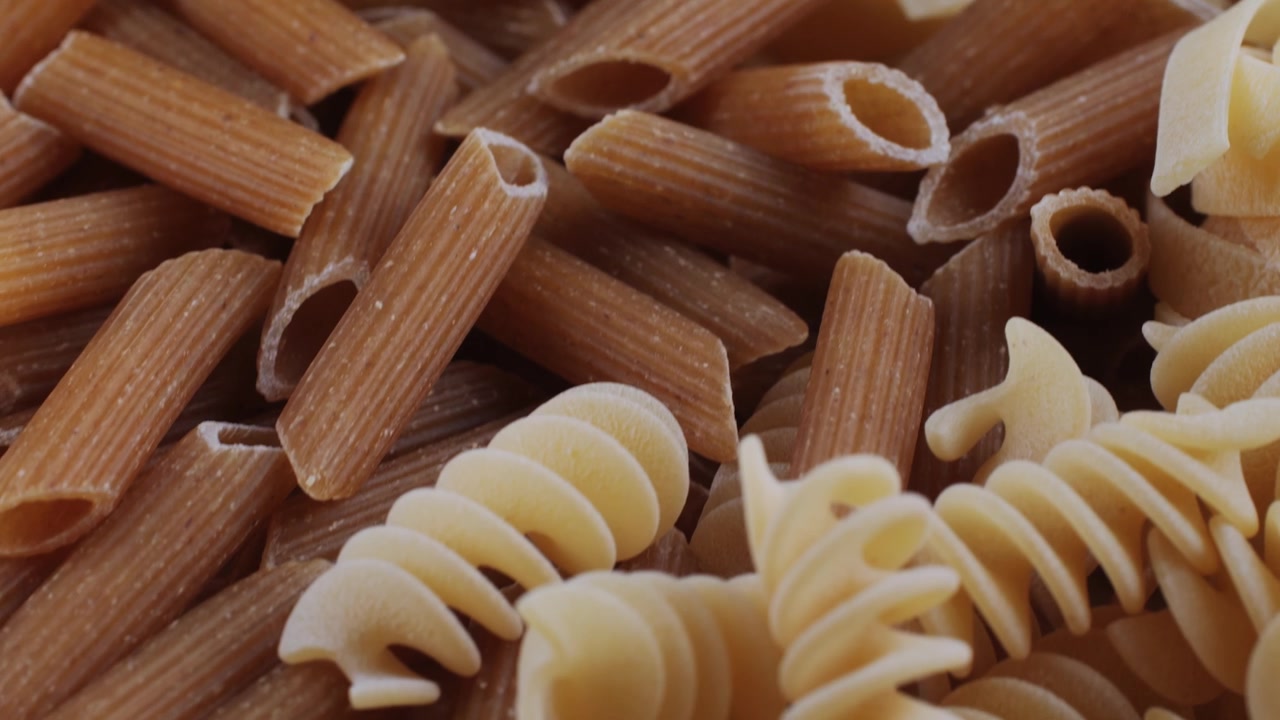 Primo piano di vari formati di pasta cruda, inclusi penne, fusilli e tagliatelle