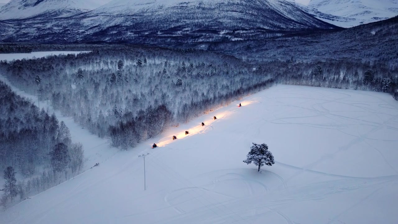 Moottorikelkat ekoturismiretkellä lumisessa maisemassa. Ilmakuva.