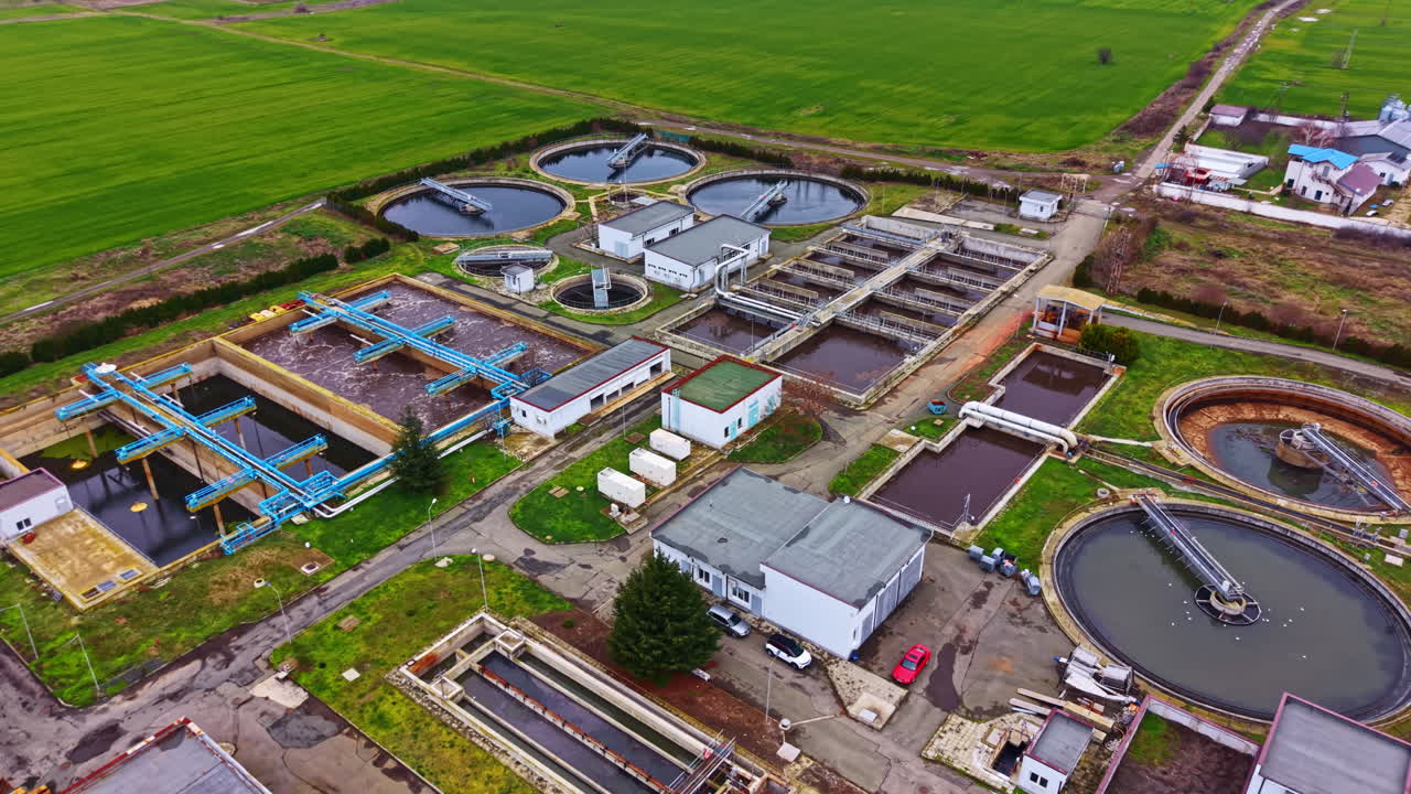 Water treatment facility processes wastewater in a rural area during daylight with various treatment tanks and buildings visible