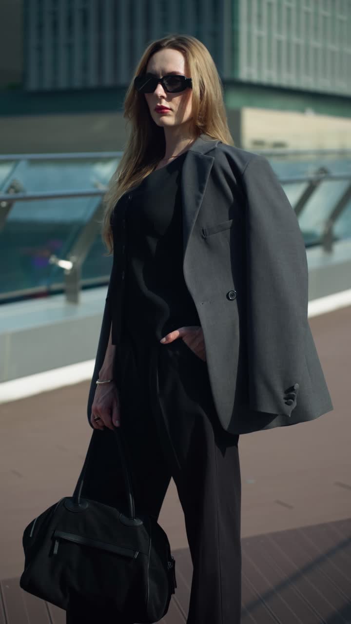 Confident businesswoman in a black suit stands on a modern office terrace at sunset, looking at the camera
