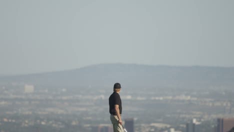 Weit-Nach-Unten-Geneigter-Blick-Auf-Einen-Golfer,-Der-Auf-Einem-Golfplatz-Mit-Bergen-Und-Einer-Stadt-Im-Hintergrund-Geht