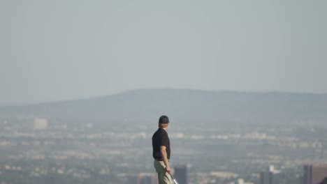 amplia vista inclinada hacia abajo de un golfista caminando en un campo de golf con montañas y una ciudad en el fondo