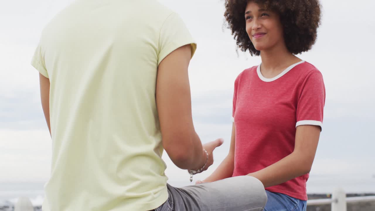 pareja afroamericana sonriendo mientras hablan entre sí sentados en un banco en el paseo marítimo