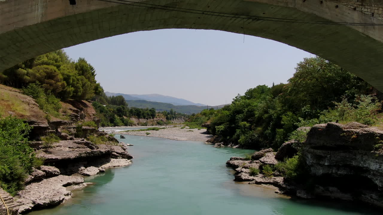 Mavi, berrak bir nehre sahip köprünün altından geçen havadan drone görüntüsü.