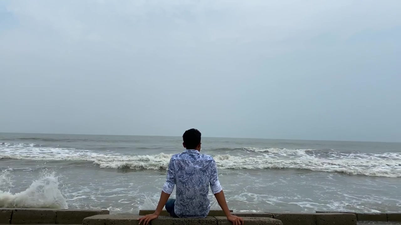 Uomo solitario e depresso che si rilassa in riva al mare mentre dolci onde lambiscono la costa con il maltempo - inquadratura statica