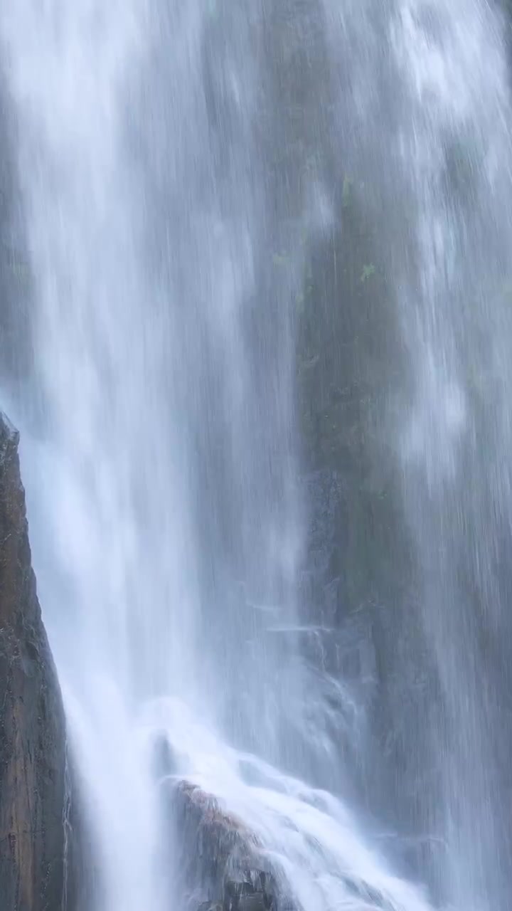 Cascada fluye sobre rocas escarpadas, con niebla que se eleva, bajo una suave luz natural y un ángulo de cámara estable.