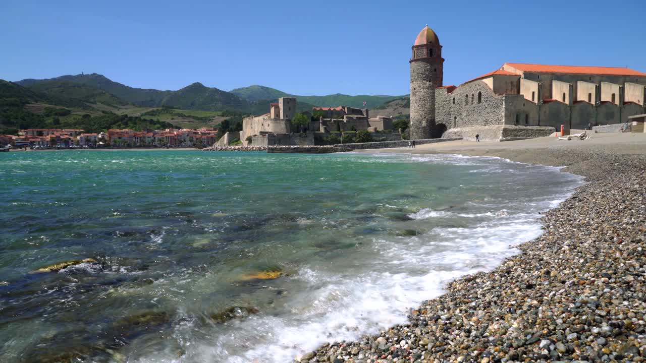 Onde lambiscono la tranquilla spiaggia di ciottoli nella baia di Collioure in una calda e ventosa giornata estiva
