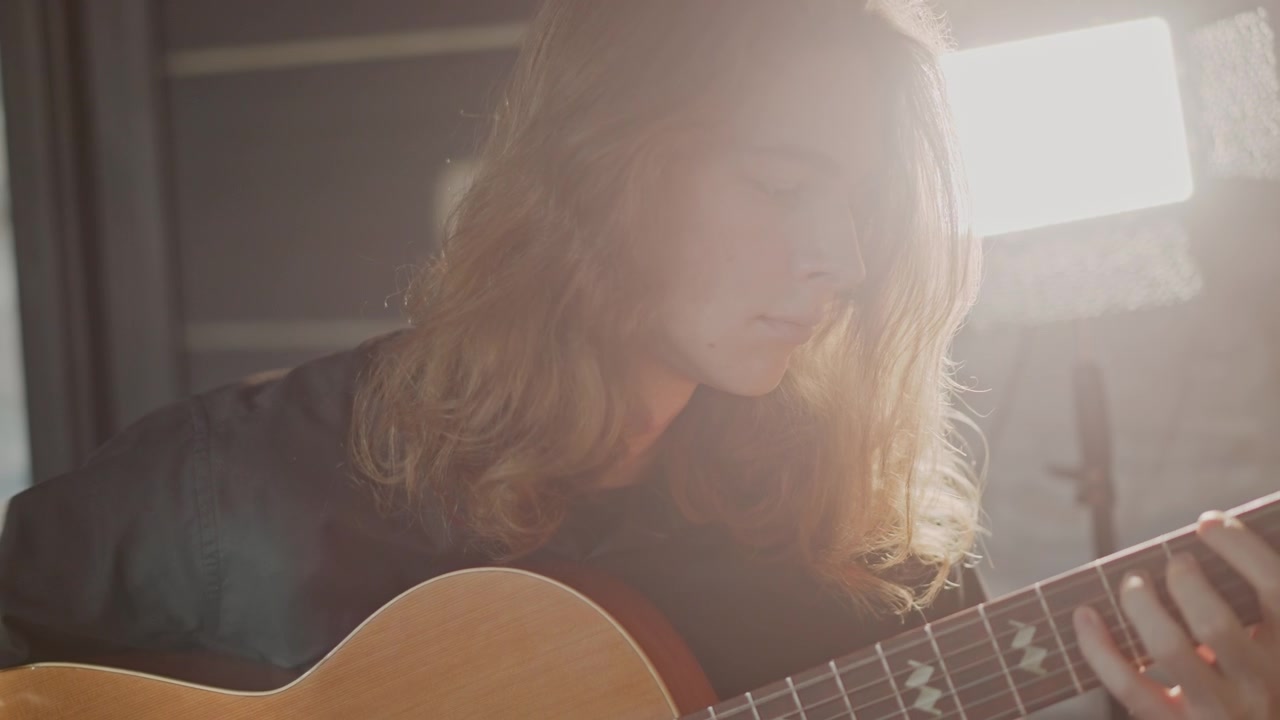 Introspektiv kaukasisk guitarist komponerer på guitar, blødt filmisk baggrundslys og lampeskær, nærbillede i profil, langsom fingerpicking, følelsesladet frasering og fokuseret udtryk, stille kreativitet