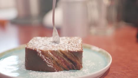 close up of a piece of cake on a plate topped with powdered sugar and a fork