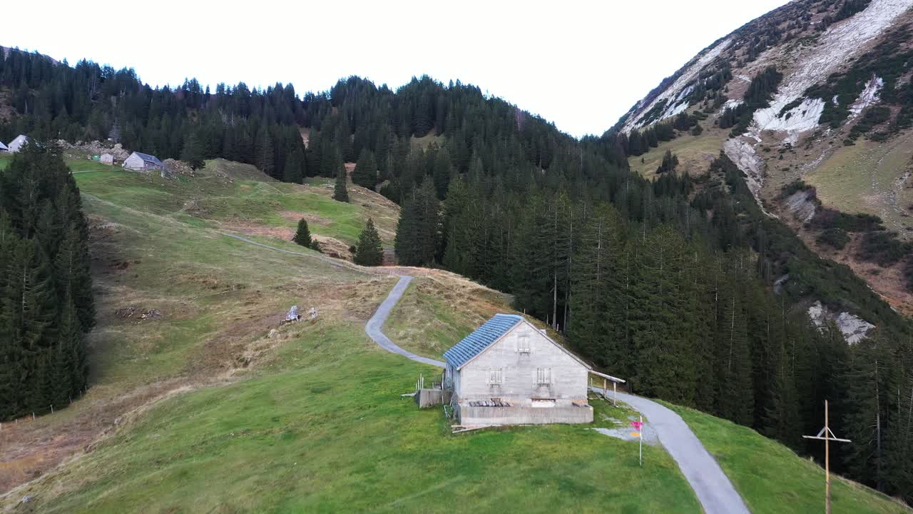 dolly delante de un excursionista caminando por una montaña lejos de una pequeña cabaña en los alpes suizos