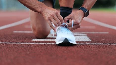 Runner-ties-his-sports-shoes-to-start-training-on-running-track,-close-up