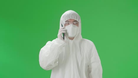 asian man wearing personal protective equipment uniform ppe, medical face mask and talking on mobile phone in the green screen studio