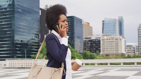 african american businesswoman holding takeaway coffee and talking on smartphone