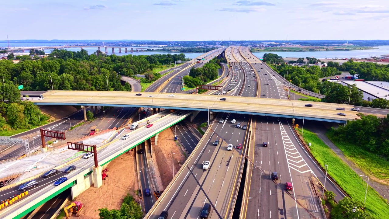 Highway interchange and green forest, United States. Overhead view of road network, moving vehicles, trees and river under clear sky. Garden State Parkway.