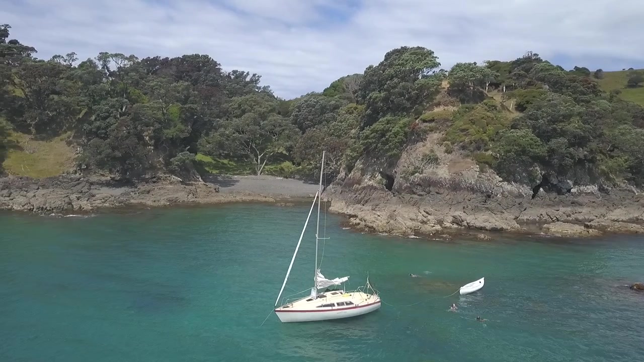 La barca che gira sul mare blu e trasparente con alcune persone che nuotano intorno, Isola di Waiheke, Nuova Zelanda