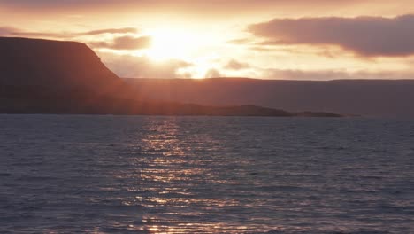 The-sun-sets,-casting-warm-light-over-the-landscape,-and-is-reflected-on-the-rippled-lake's-surface-in-a-timelapse-video