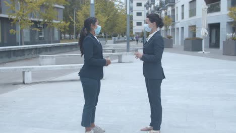 business colleagues in face masks meeting at office building, greeting each other with elbows bumps and talking