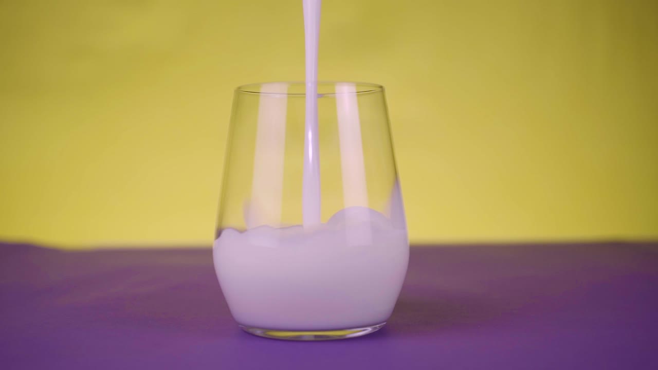 Healthy eating, diet and drinks concept. Milk pouring in a glass in slow motion on purpple-yellow background