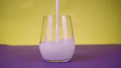 healthy eating, diet and drinks concept. milk pouring in a glass in slow motion on purpple-yellow background