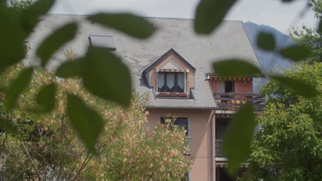 a pink house with a slate roof seen through the branches of trees