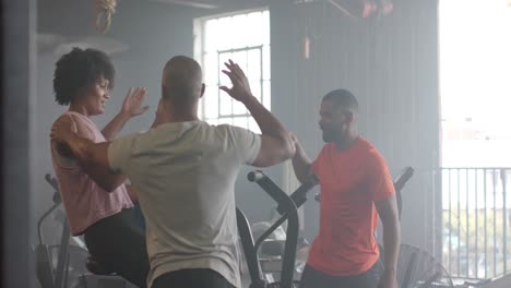 Diverse-group-fitness-class-high-fiving-after-training-on-elliptical-bikes-at-gym,-in-slow-motion