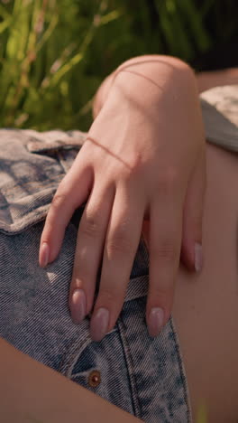primer plano de una mujer joven acostada en un campo cubierto de hierba con la mano apoyada en su estómago, la luz del sol proyecta sombras suaves sobre su forma relajada, el sol se refleja cálidamente en su mano