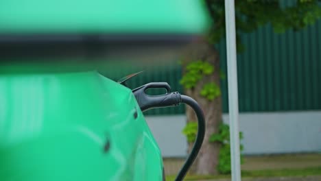 green electric car plugged in during slow motion left slide in natural setting