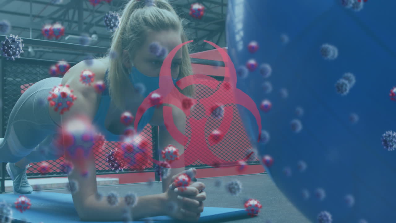 символ биологической опасности и клетки covid-19 против женщины в маске, выполняющей упражнение на доске в тренажерном зале