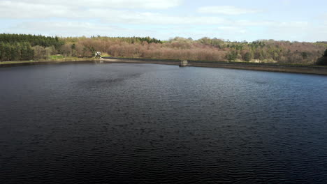 aerial flyover of fewston reservoir zooming in to reveal lakeside house with car crossing dam