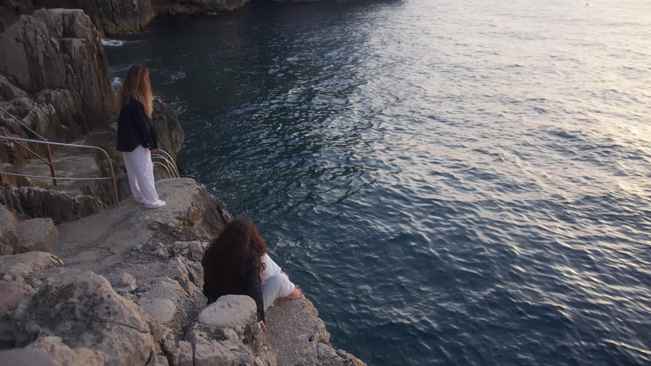Two Women Relaxing on a Cliff Overlooking the Calm Ocean