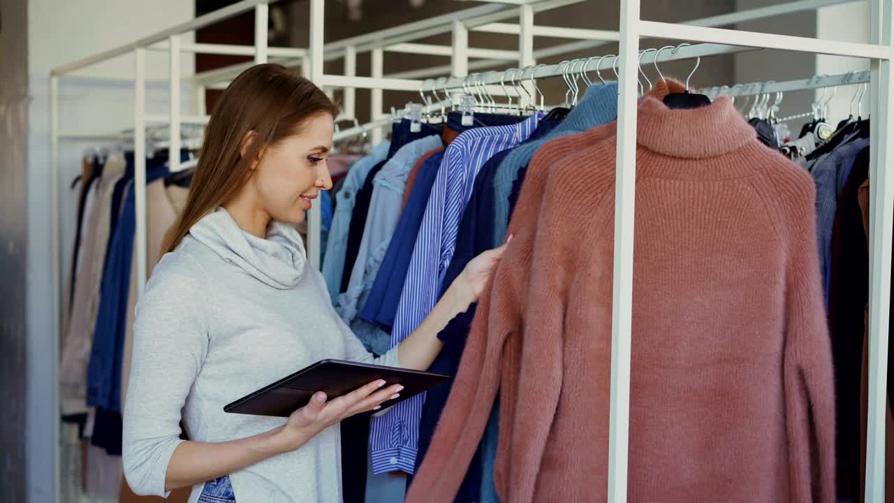 la propietaria de una tienda de ropa para mujeres está comprobando y contando prendas de vestir en los rieles mientras usa una tableta. está escribiendo información sobre sus bienes. concepto de pequeña empresa.