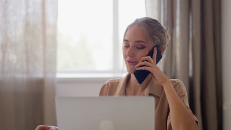 Woman-talk-on-mobile-phone-near-laptop-at-white-table