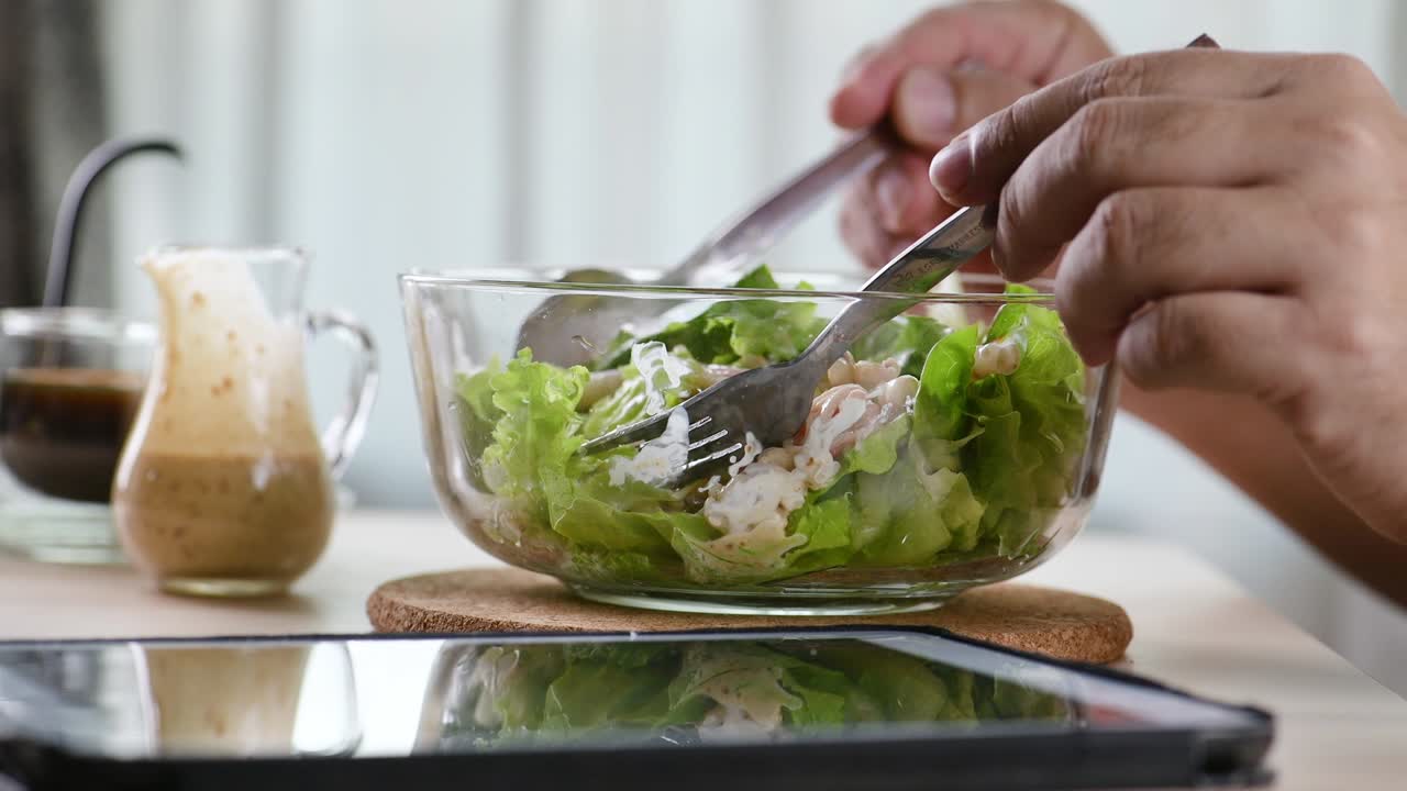아내는 아침 식사 테이블에서 남편에게 초록색 채소 러드 한 그을 제공합니다. 신선한 러드를 먹고 깨한 채소가 생으로 먹을 수 있습니다. 음식을 먹고, 커피를 마시고, 터치 스크린 태블릿 컴퓨터 태블릿을 보고 슬라이드를 표시합니다.