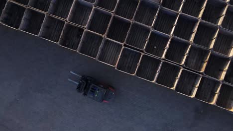 imágenes de drones de una carretilla elevadora conduciendo sin carga junto a una pila de paletas a la luz del día
