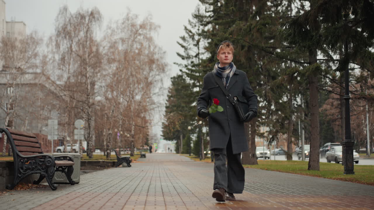 Creatore caucasico che tiene una rosa rossa in un parco, ritratto ravvicinato, cappotto scuro e guanti, passo delicato, si avvicina a una panchina, sguardo desideroso, gesto poetico, atmosfera romantica, il creatore come poeta che offre un dono.