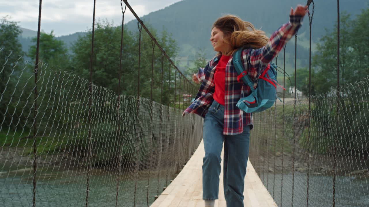 Viaggiatore felice che salta in montagna su un ponte fluviale. Donna emozionata che cammina durante un'escursione.