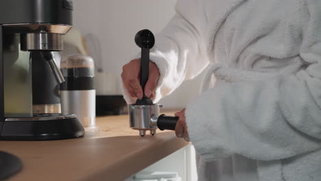 mujer tocando café en un primer plano de portafilter. dama con bata de baño suave llena el recipiente con polvo de espresso en casa. preparación de bebidas energéticas