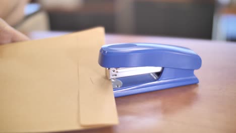 Hands-binding-envelope-with-stapler,-office-workspace-essential-tool-close-up
