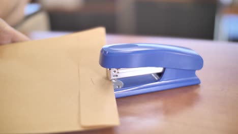 hands binding envelope with stapler, office workspace essential tool close up