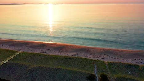 Vista-Aérea-Por-Drones-De-La-Puesta-De-Sol-Sobre-La-Casa-De-Playa-En-Saco-Maine-Con-Colores-Reflejados-En-Las-Olas-Del-Océano-Y-Casas-De-Vacaciones-A-Lo-Largo-De-La-Costa-Atlántica-De-Nueva-Inglaterra