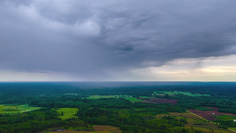 an aerial timelapse captures dramatic grey storm clouds moving quickly over a vast latvian landscape of dense green forests and agricultural fields, signaling impending rain