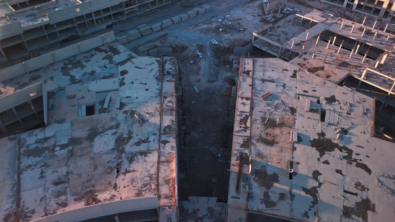 Vista aerea cinematografica di una struttura circolare in cemento abbandonata e incompiuta con colonne a vista, detriti e pozzanghere sul tetto durante l'ora d'oro: ideale per temi riguardanti degrado urbano, riqualificazione e costruzione