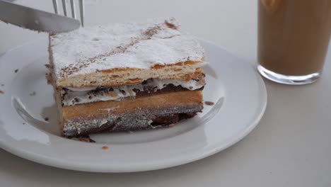 Close-up-woman-hands-cutting-piece-of-millefeuille-with-knife-and-fork