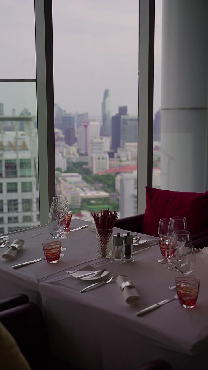 Puesta de mesa elegante en restaurante de altura con vista panorámica del horizonte de Bangkok, Tailandia. 4K vertical