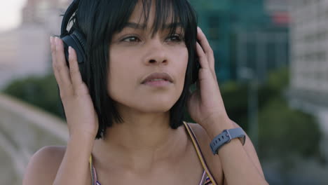 retrato en primer plano hermosa joven mujer hispana que mira con confianza a la cámara se pone auriculares escuchando música disfrutando de un estilo de vida urbano relajado