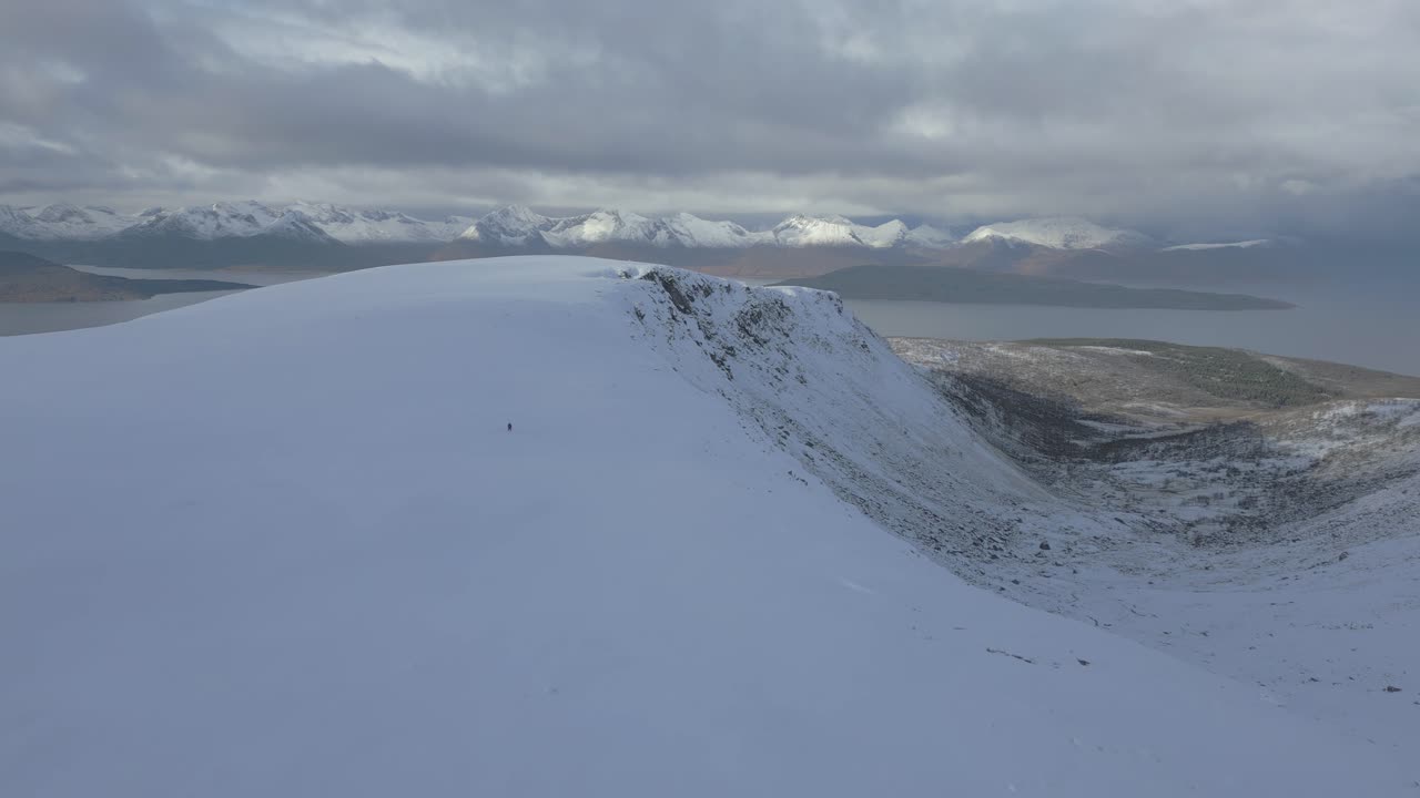 Man appears as a dot walking on vast snowy mountain landscape.