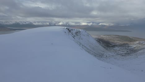 man appears as a dot walking on vast snowy mountain landscape.
